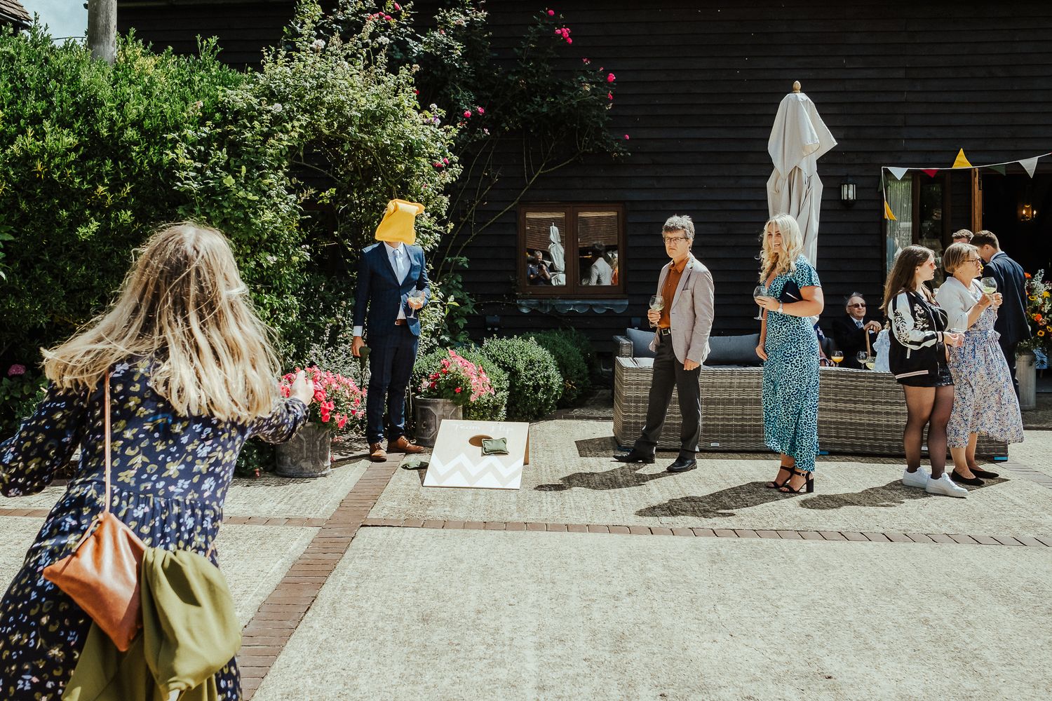 Guests gather in sunny courtyard during daytime wedding festivities.