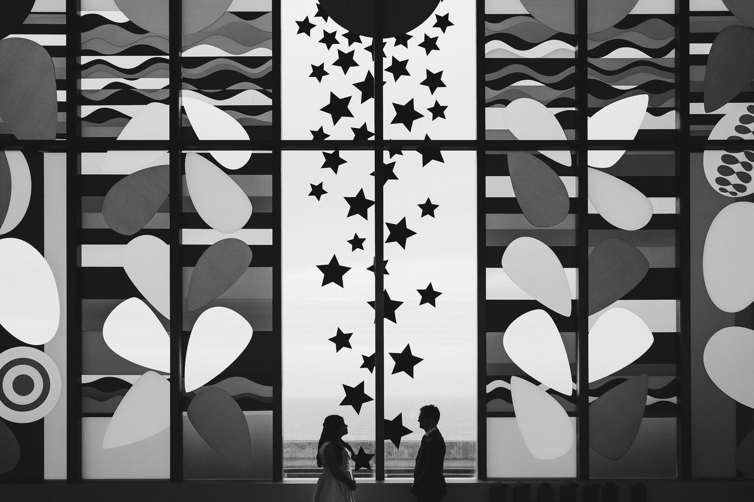 Silhouetted figures against a geometric window display with stars and heart patterns.