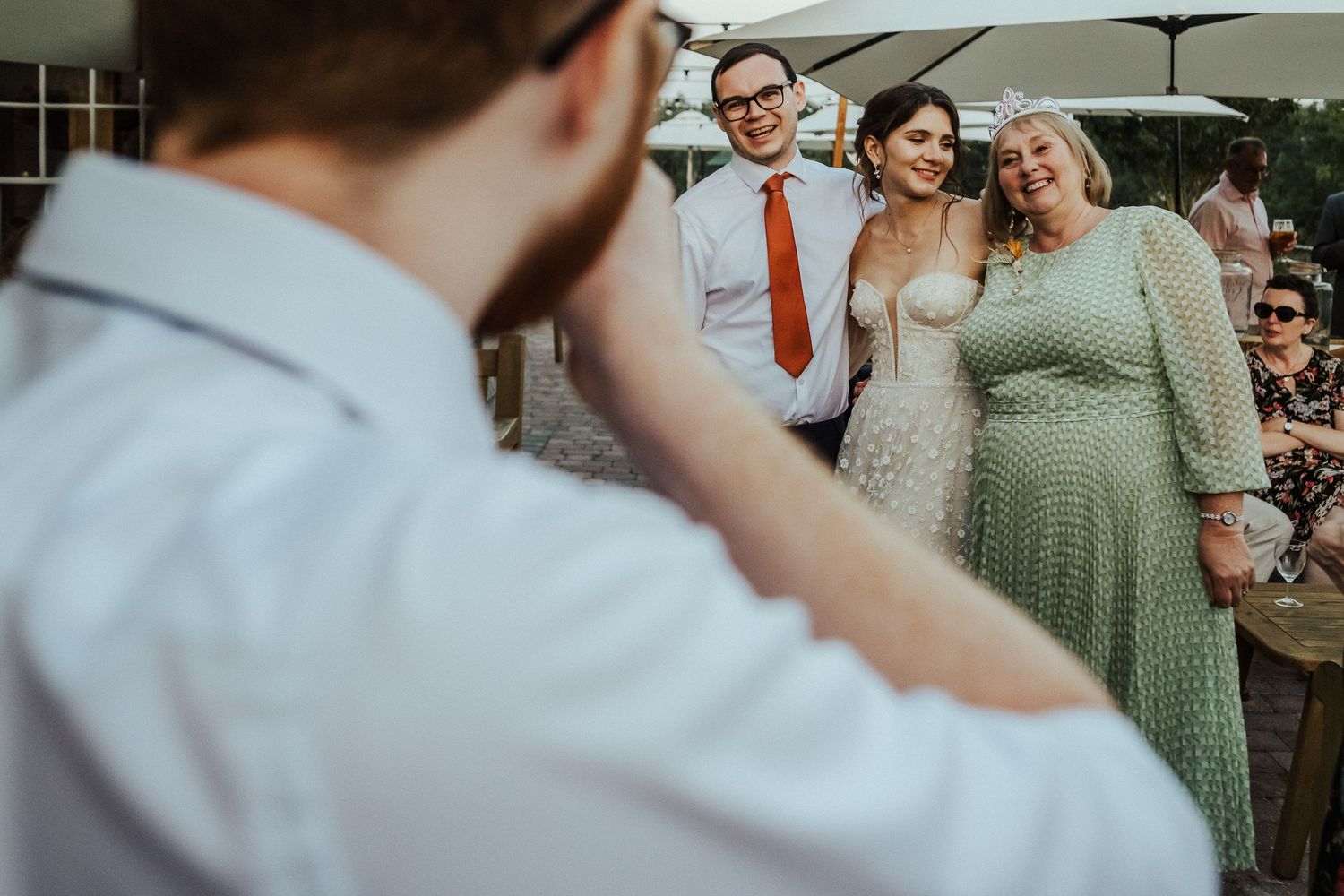 Wedding party gathers outdoors while photographer captures candid moment at summer celebration.