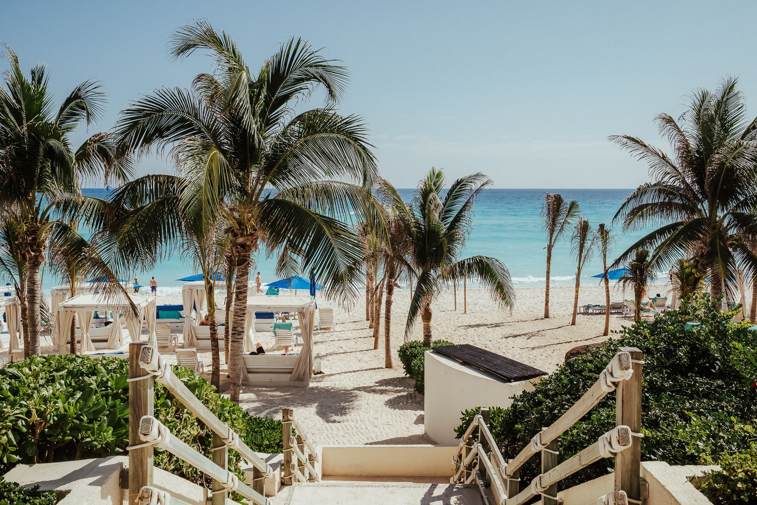 Wooden walkway leading to tropical beach with palm trees and turquoise waters.