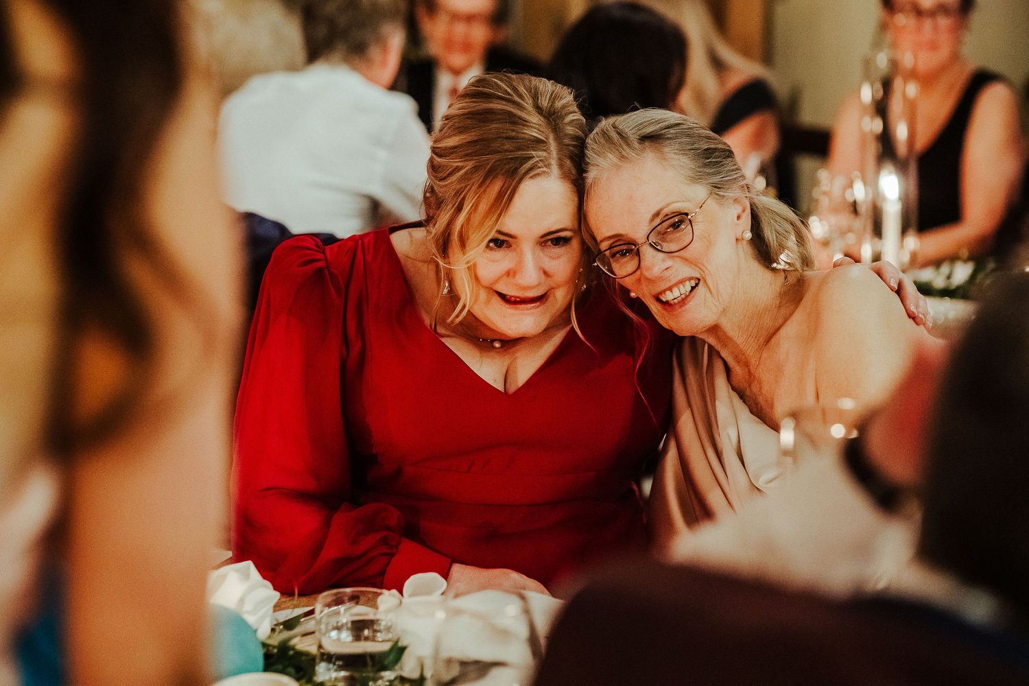Intimate gathering of friends share laughter around dining table with warm lighting.