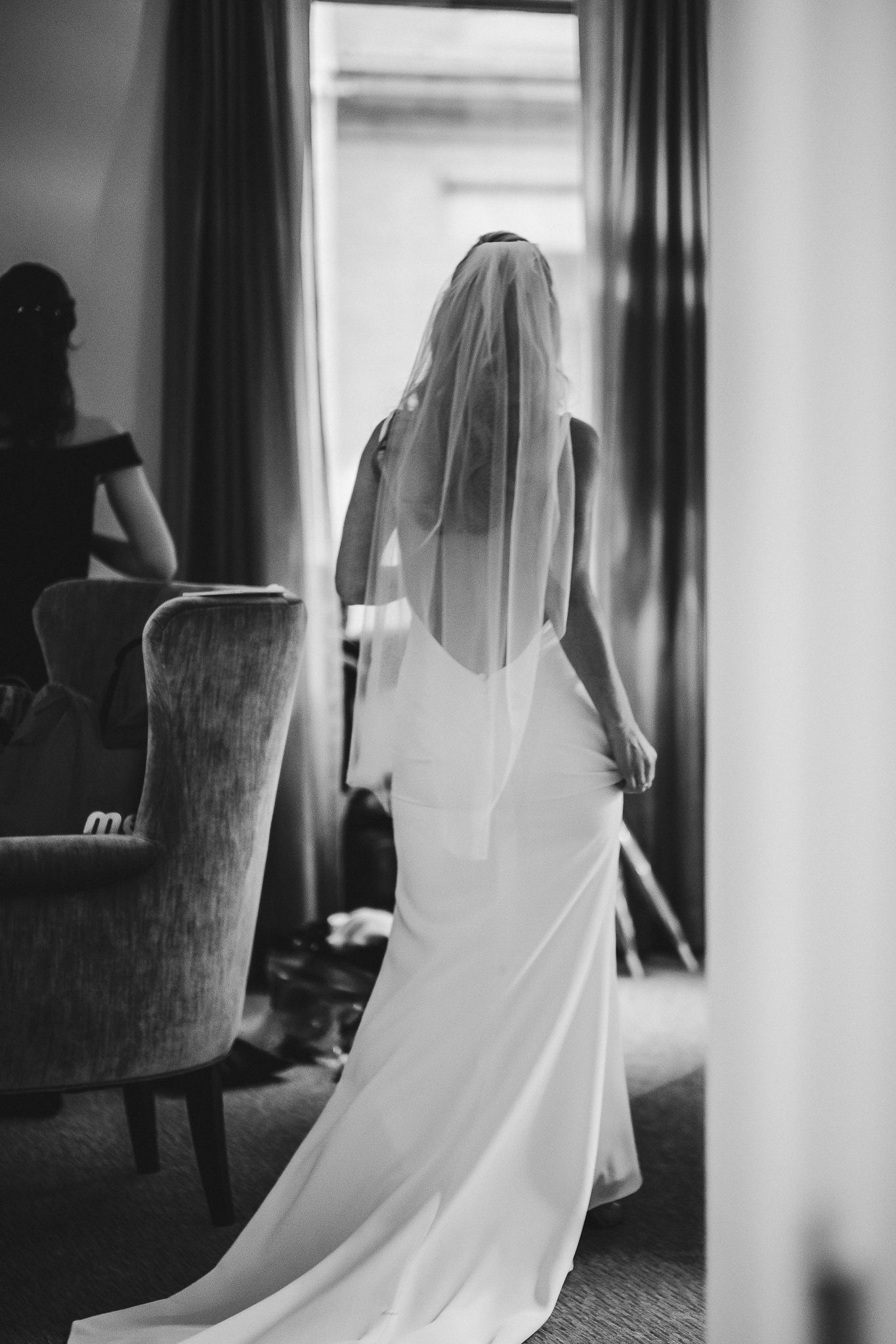 Silhouette of bride in elegant dress and veil looking in mirror during wedding preparation.