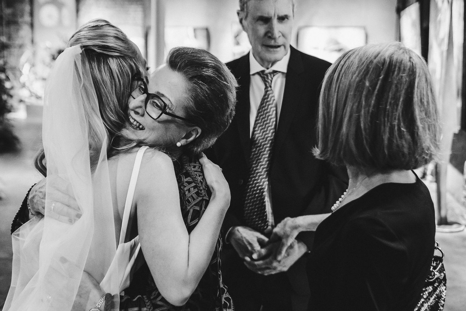Black and white moment of emotional embraces during indoor wedding celebration.