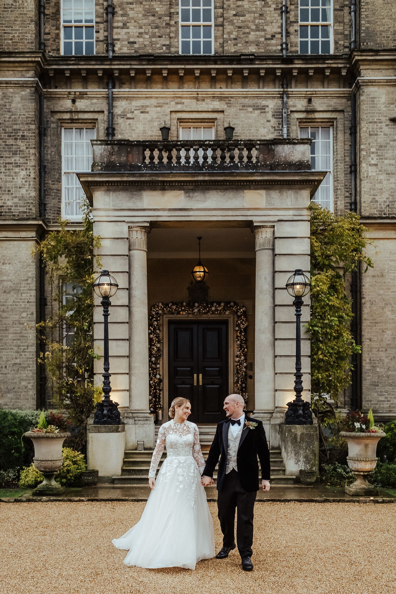 Elegant couple poses outside grand mansion entrance with classical architecture.