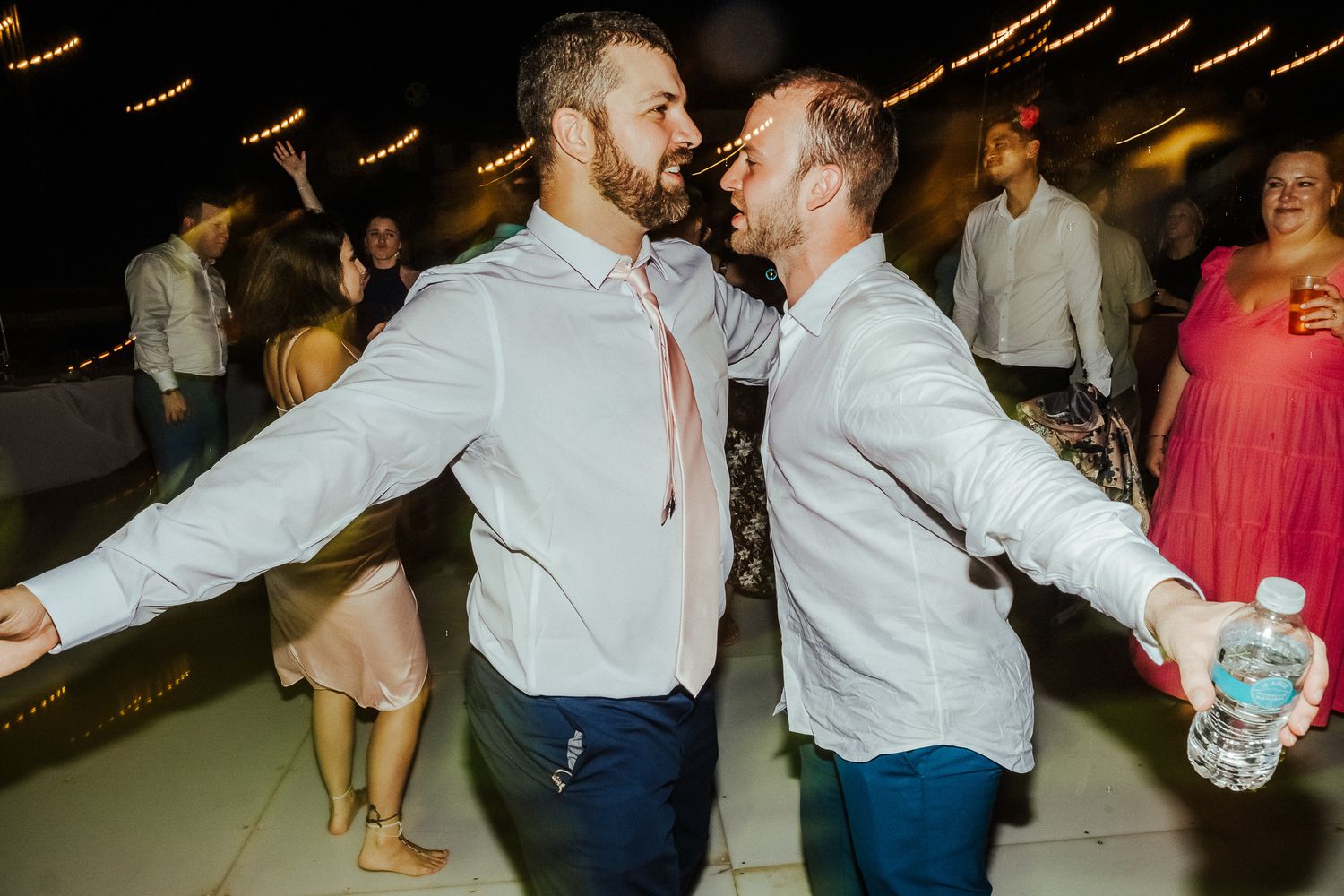 Two guests in dress shirts and ties dance energetically at an evening celebration.