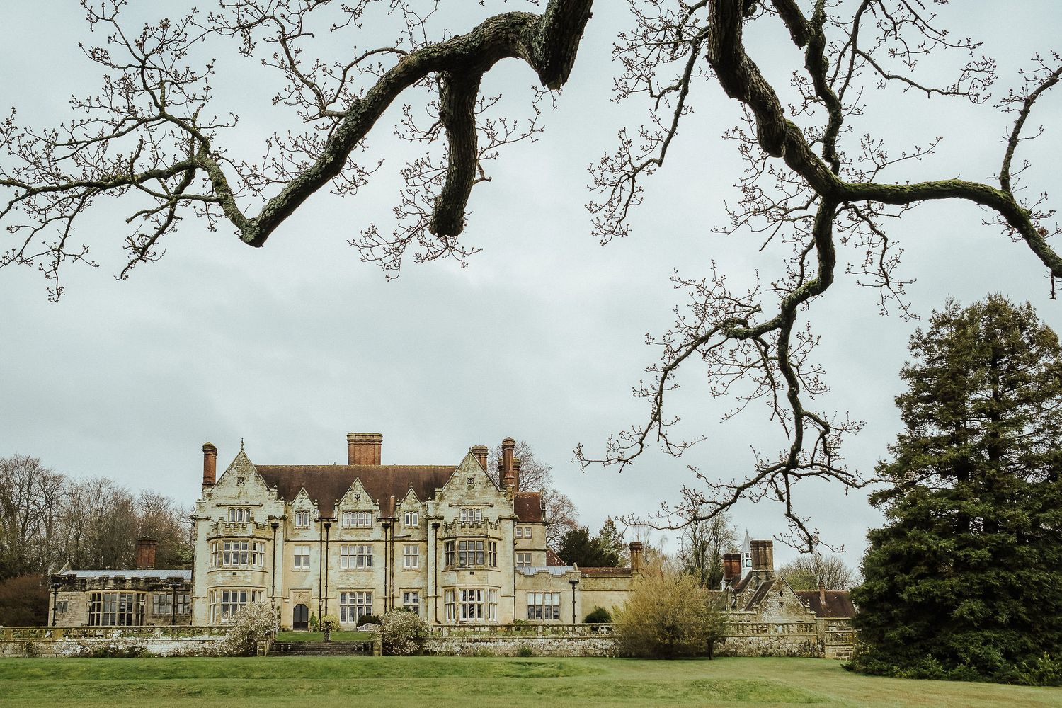 Historic mansion with Tudor-style architecture surrounded by winter trees and grounds.