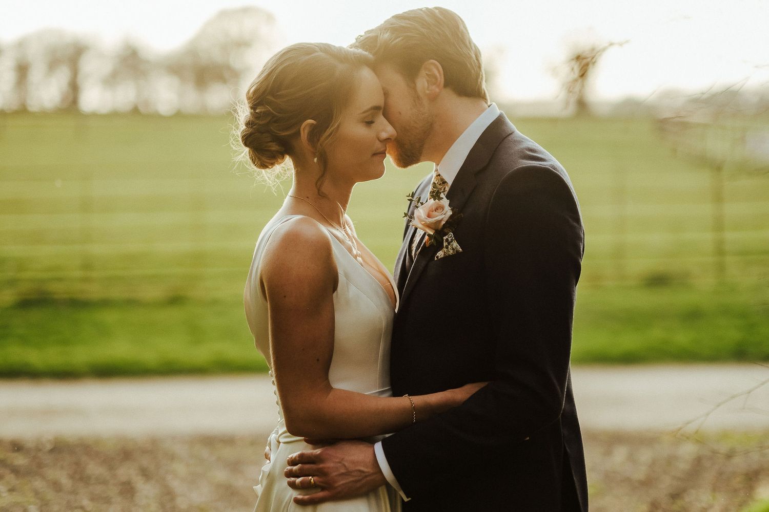 Soft golden light illuminates a romantic moment between newlyweds in an open field.