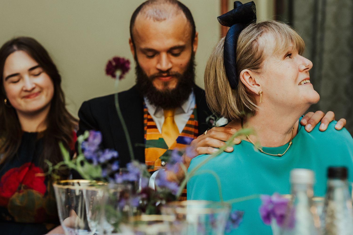 Wedding reception guests gathered around tables with drinks and flowers, sharing joyful moments together.