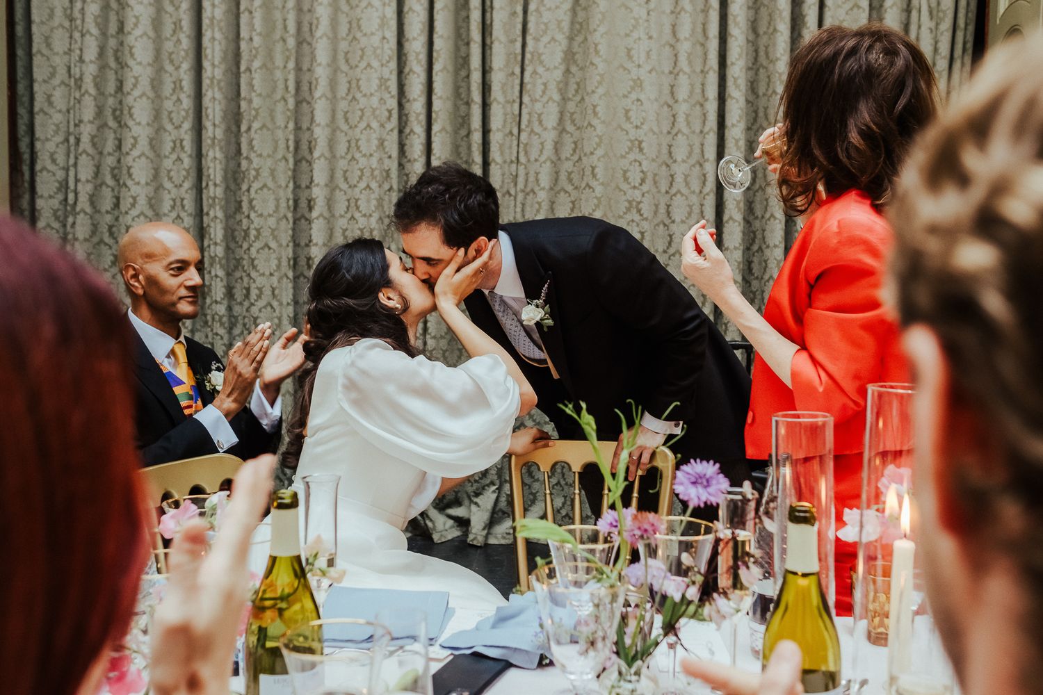 Wedding guests socializing at decorated tables with curtains in the background.
