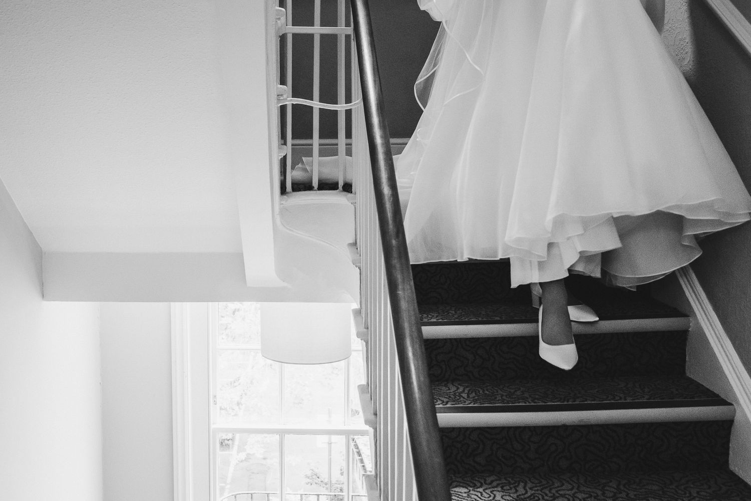 A bride's dress and shoes are visible descending elegant stairs in black and white.