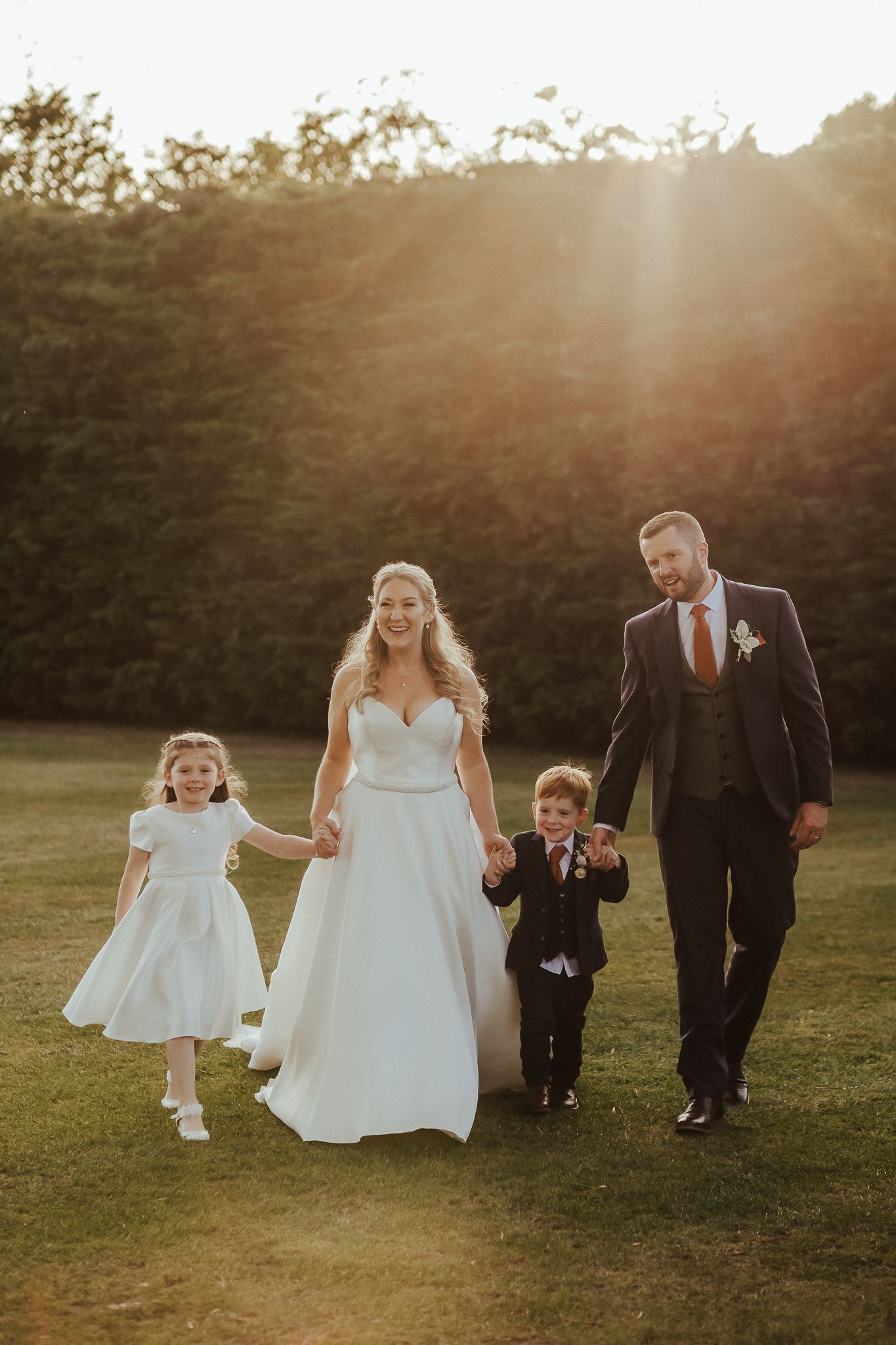 Golden sunset wedding portrait of family walking together on grassy field.
