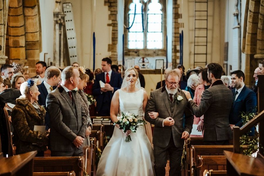 Newlyweds walking down church aisle surrounded by celebrating guests in historic setting.