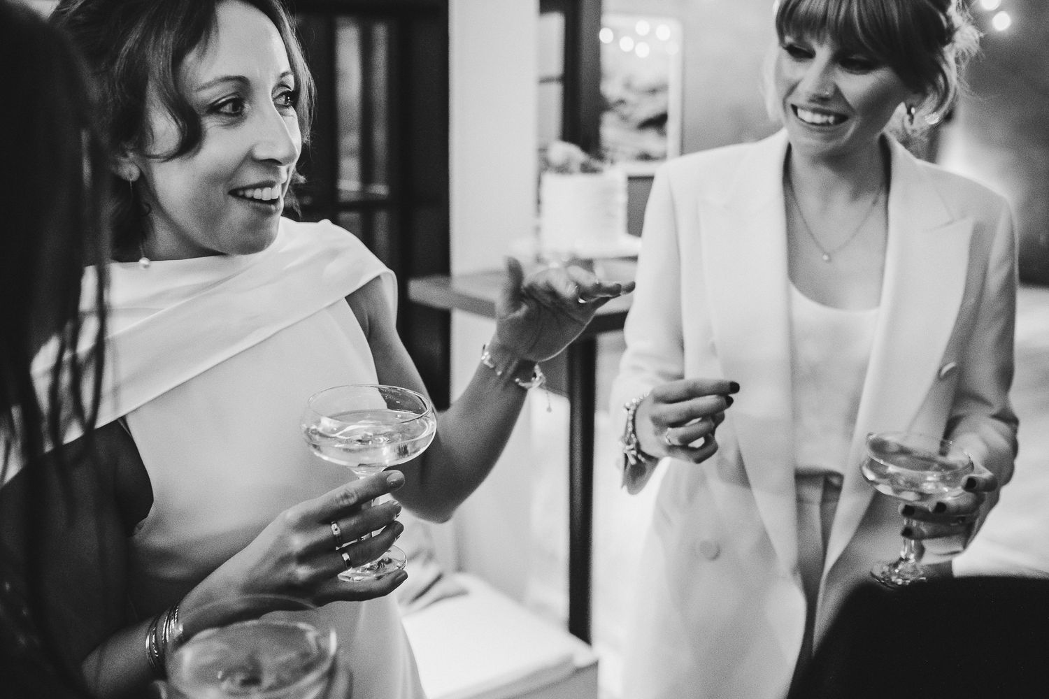 Two people in white outfits share drinks and conversation at an elegant event.