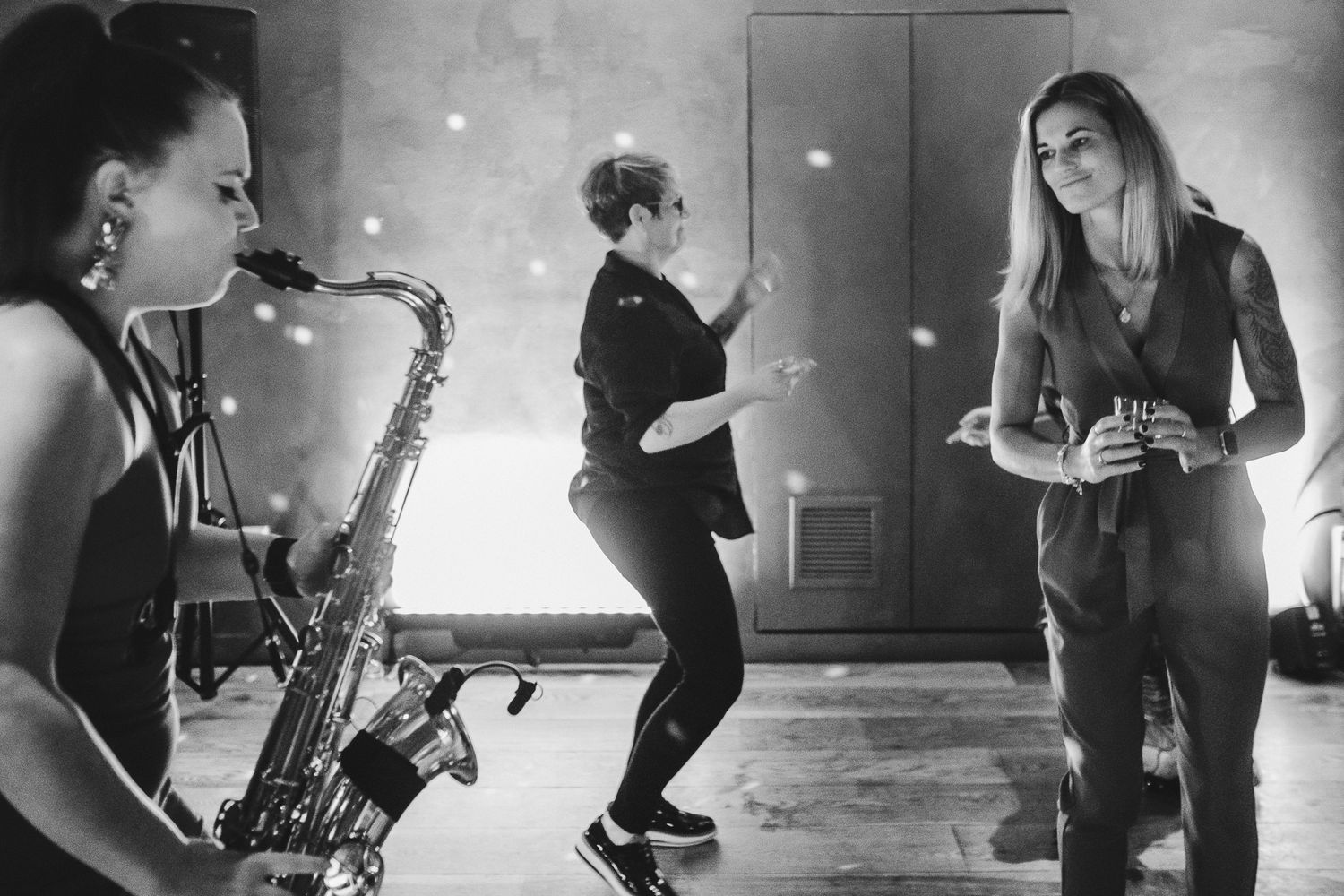 Musicians performing with saxophone while people dance in a dimly lit venue.