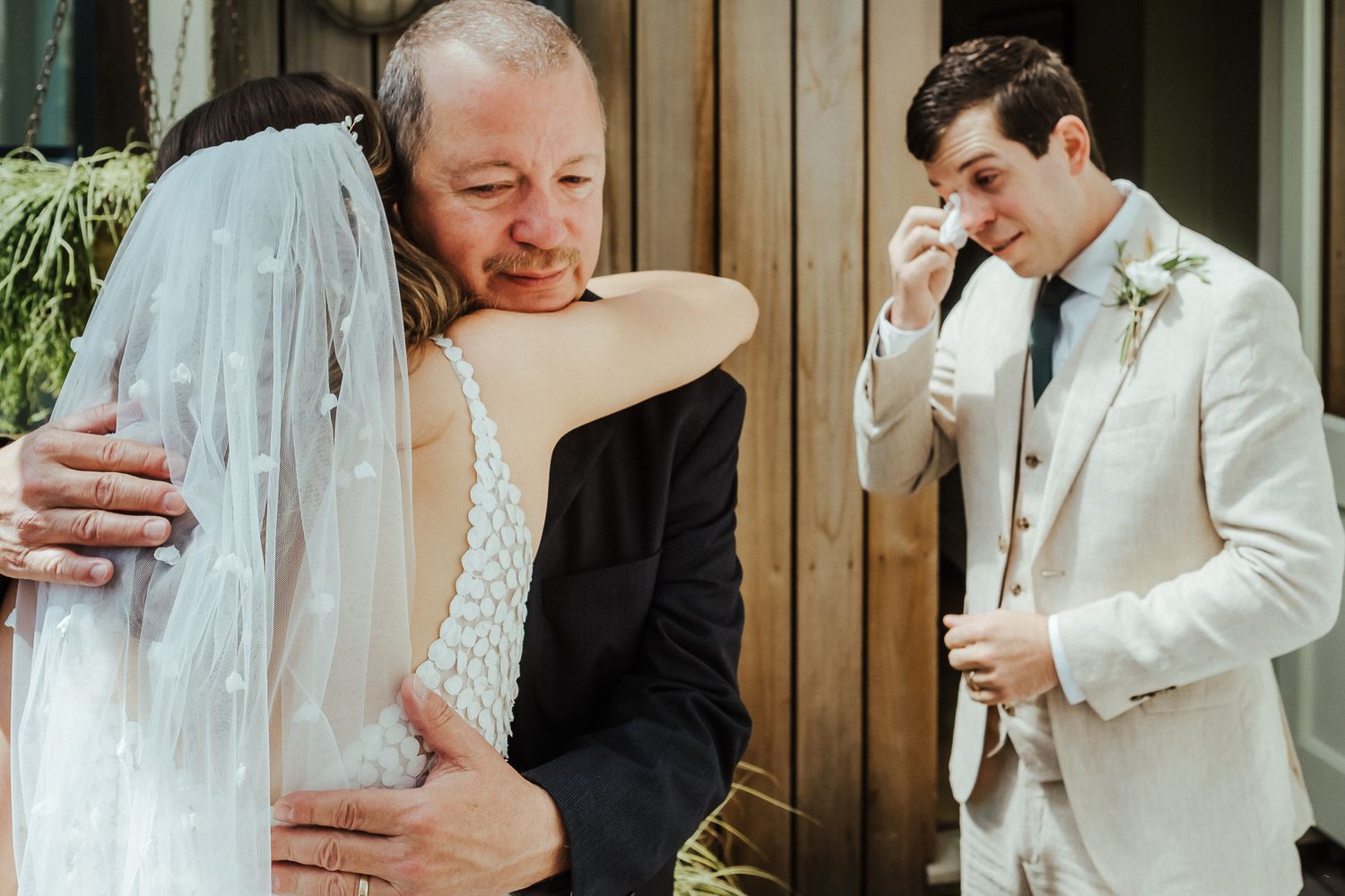An emotional moment between a bride and father figure while the groom wipes away tears.
