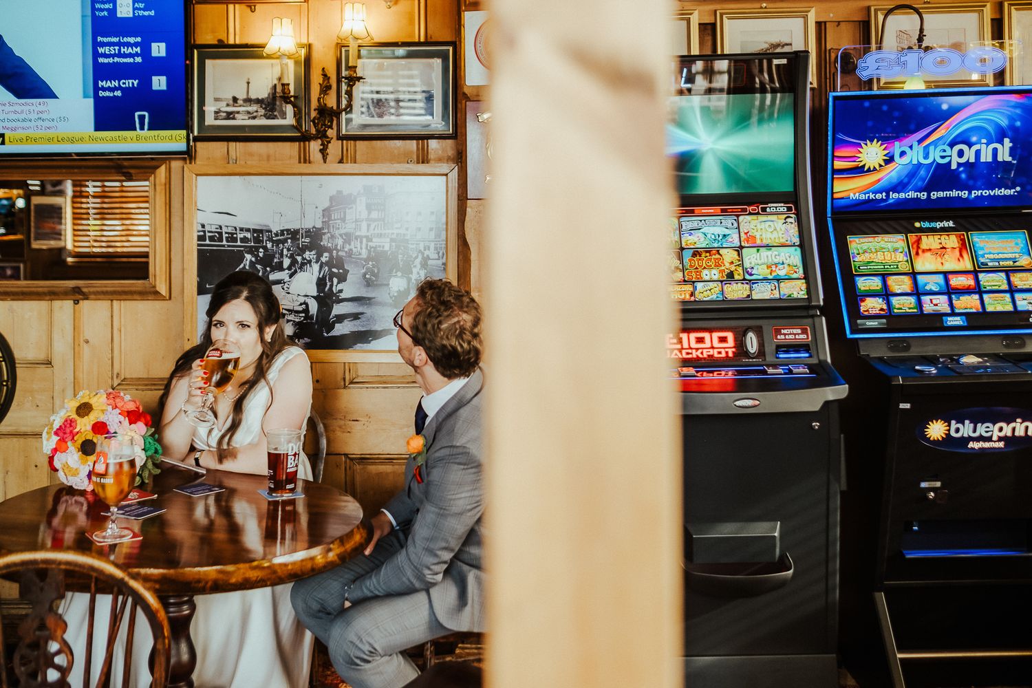 Newlyweds sharing drinks at a casual bar with slot machines in background.