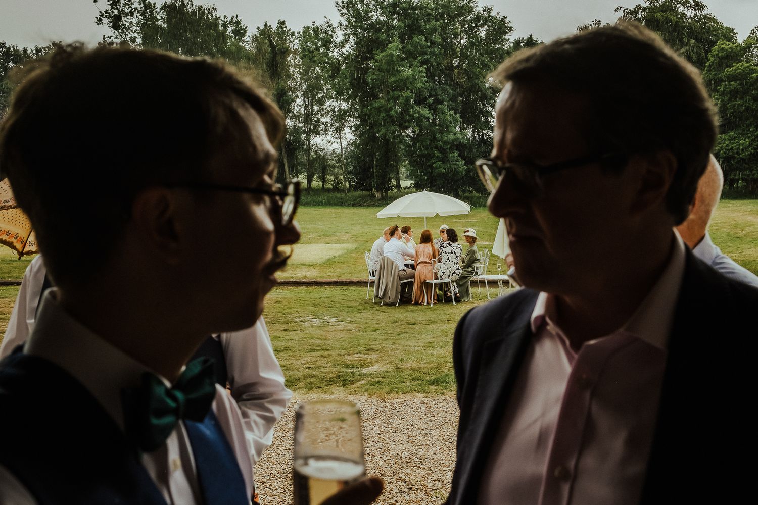 Outdoor wedding reception with guests gathered under trees at dusk.