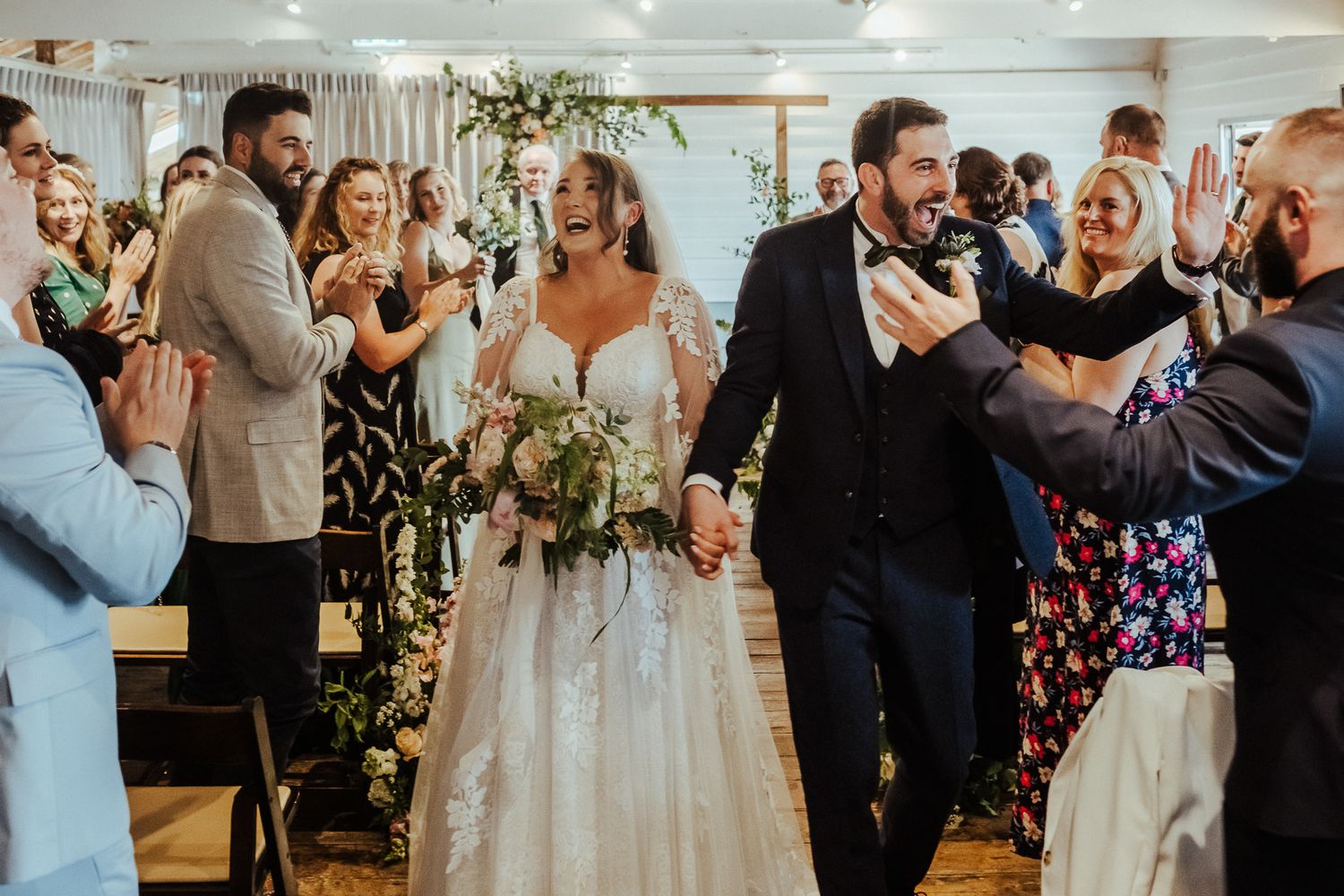 Newlyweds walk down the aisle while wedding guests cheer and applaud.