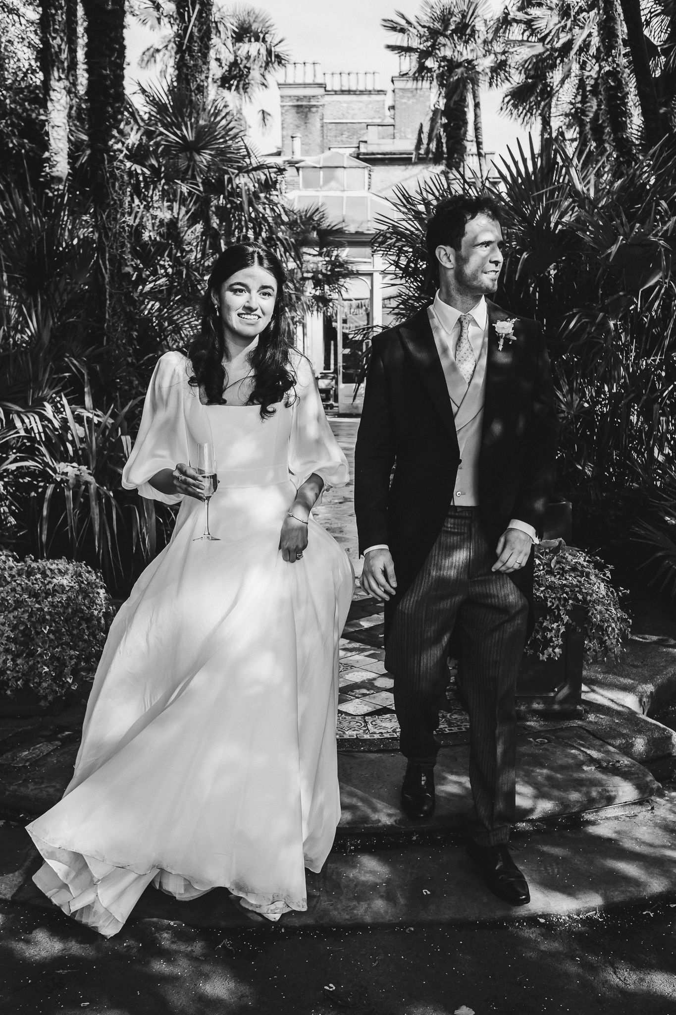 Newlyweds walking together and laughing among tropical palm trees at elegant venue.