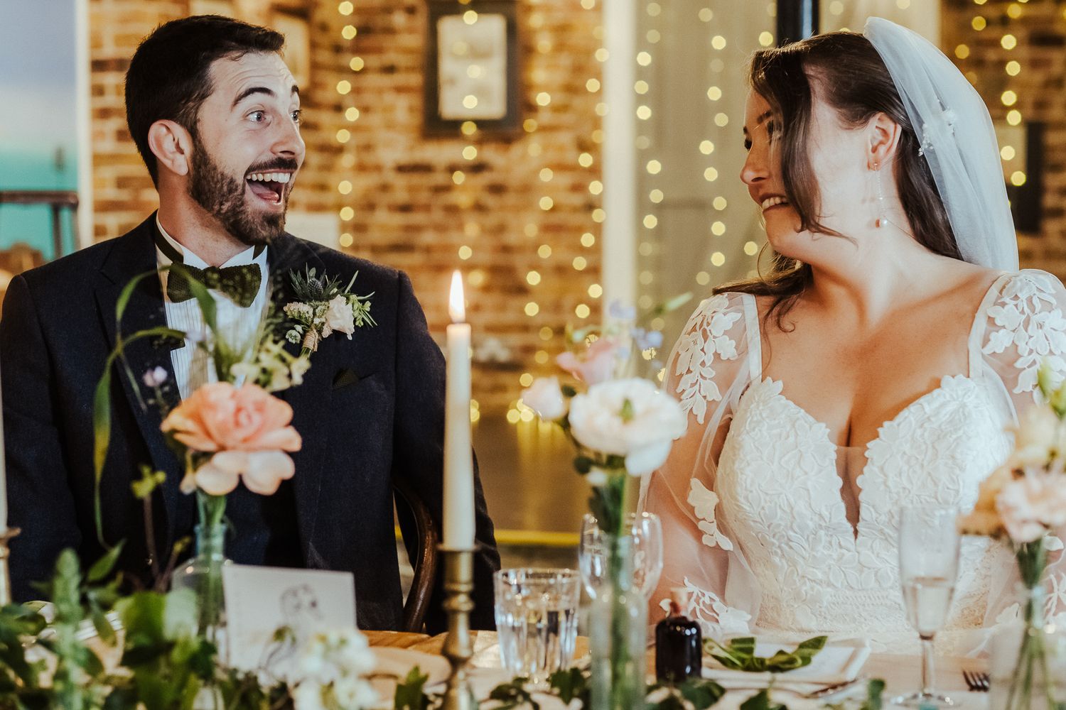 Candid moment of bride and groom sharing laughter at reception dinner table.