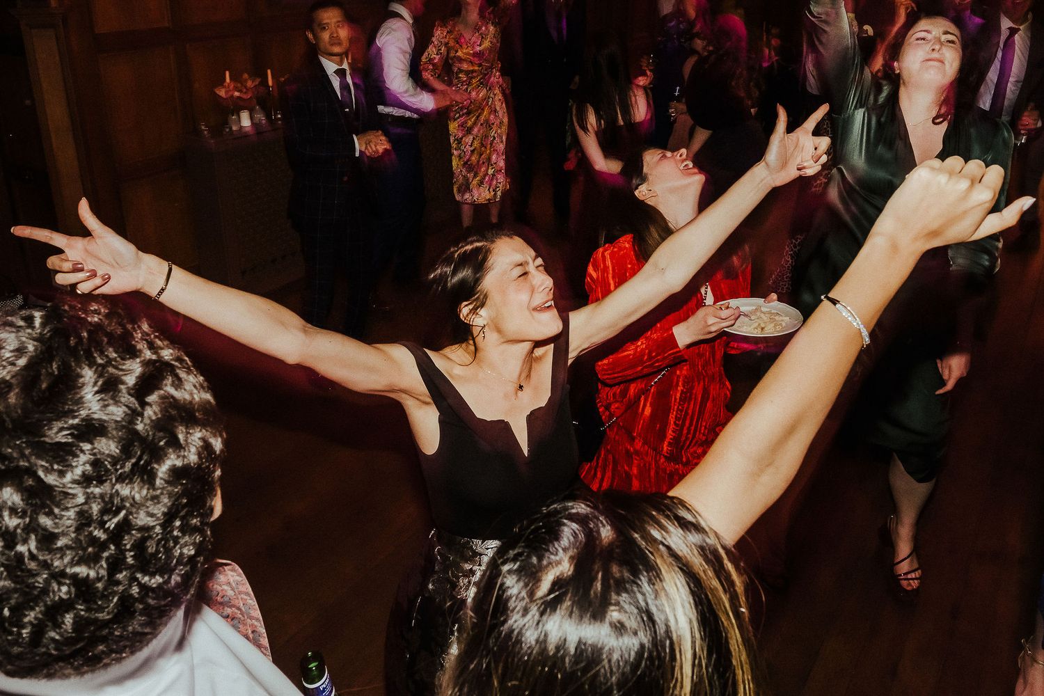 A joyful party scene with dancing guests in a dimly lit venue with dark wood paneling.