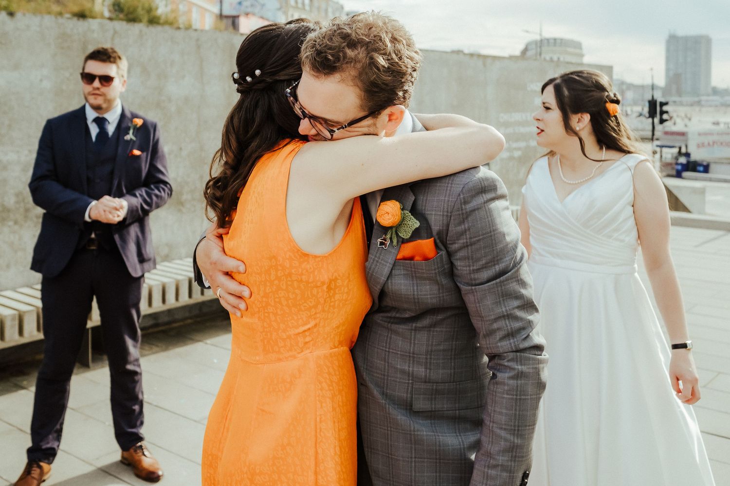 Wedding party embracing outdoors with person in bright orange dress.