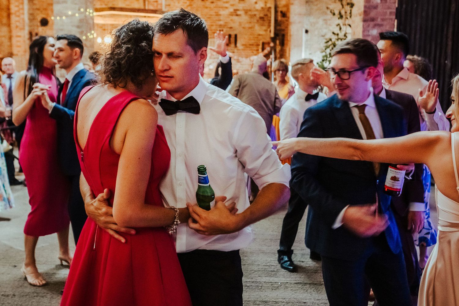 Couples dancing at an indoor wedding reception venue with brick walls.