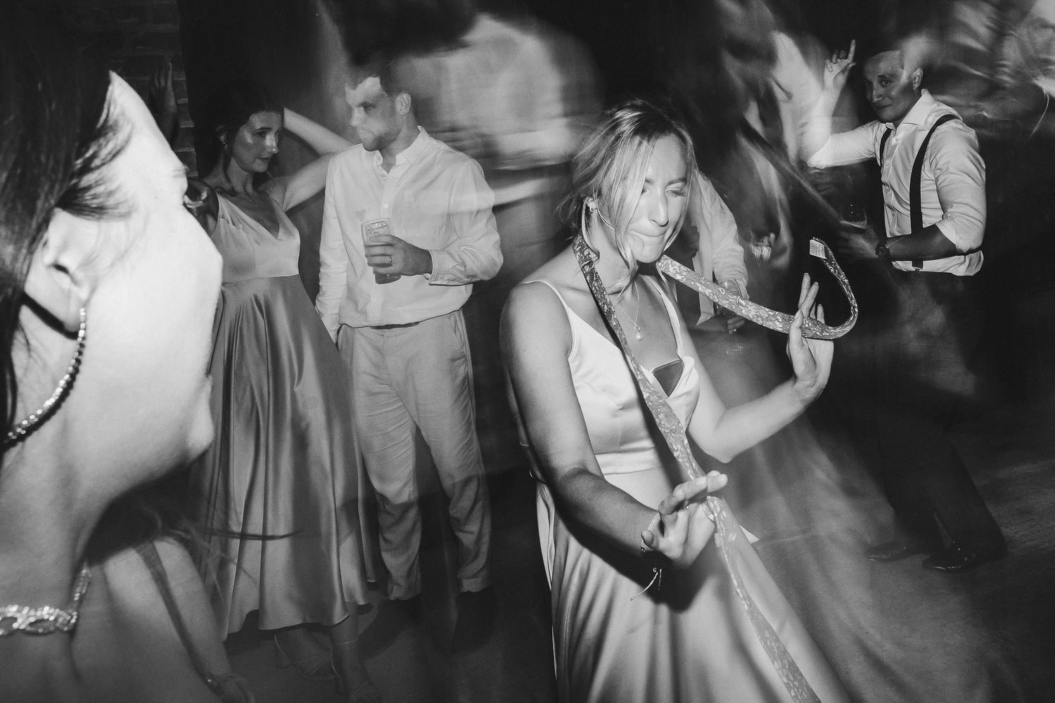 Party guests dancing energetically at a wedding reception in black and white.