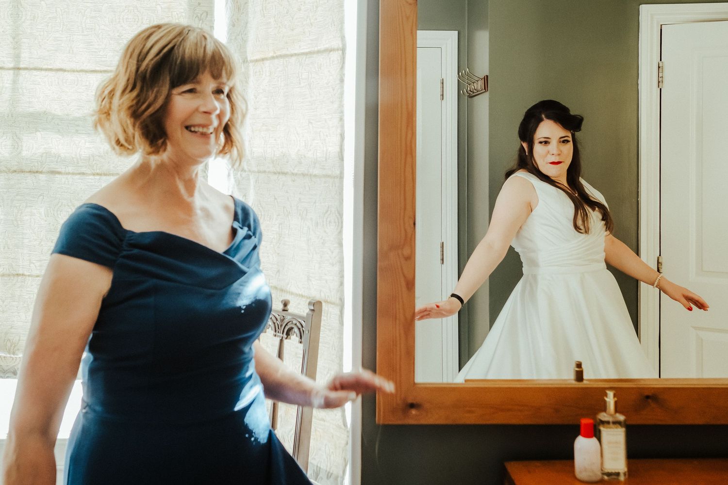 Two dresses, one navy blue and one white, are showcased in a bright room with mirrors.