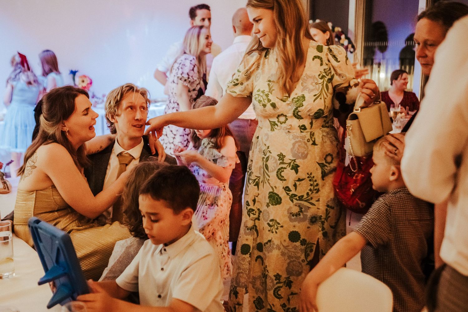 Group of party guests interact animatedly while seated at decorated tables.