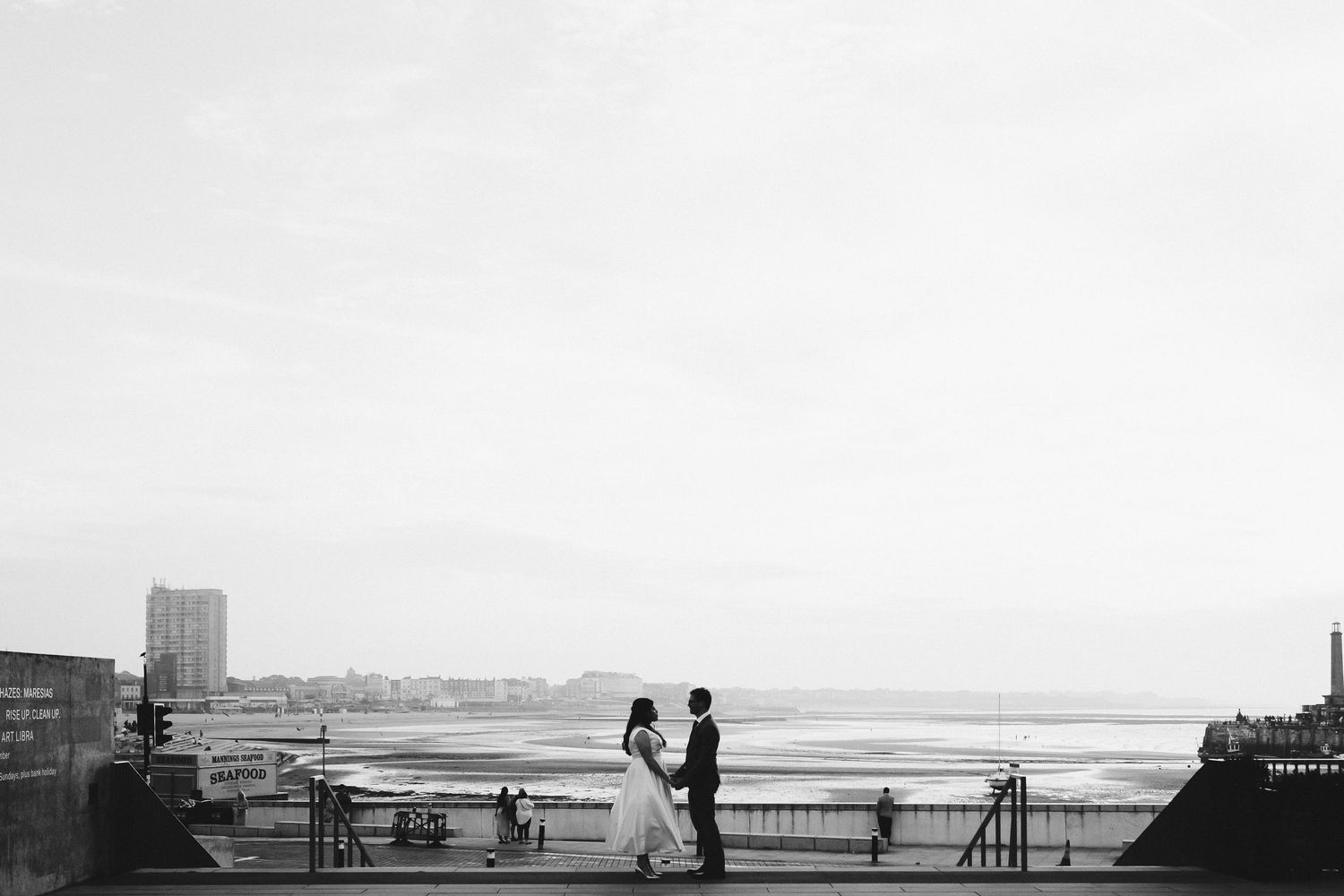 Black and white silhouette of a couple on a seaside viewpoint overlooking the ocean.