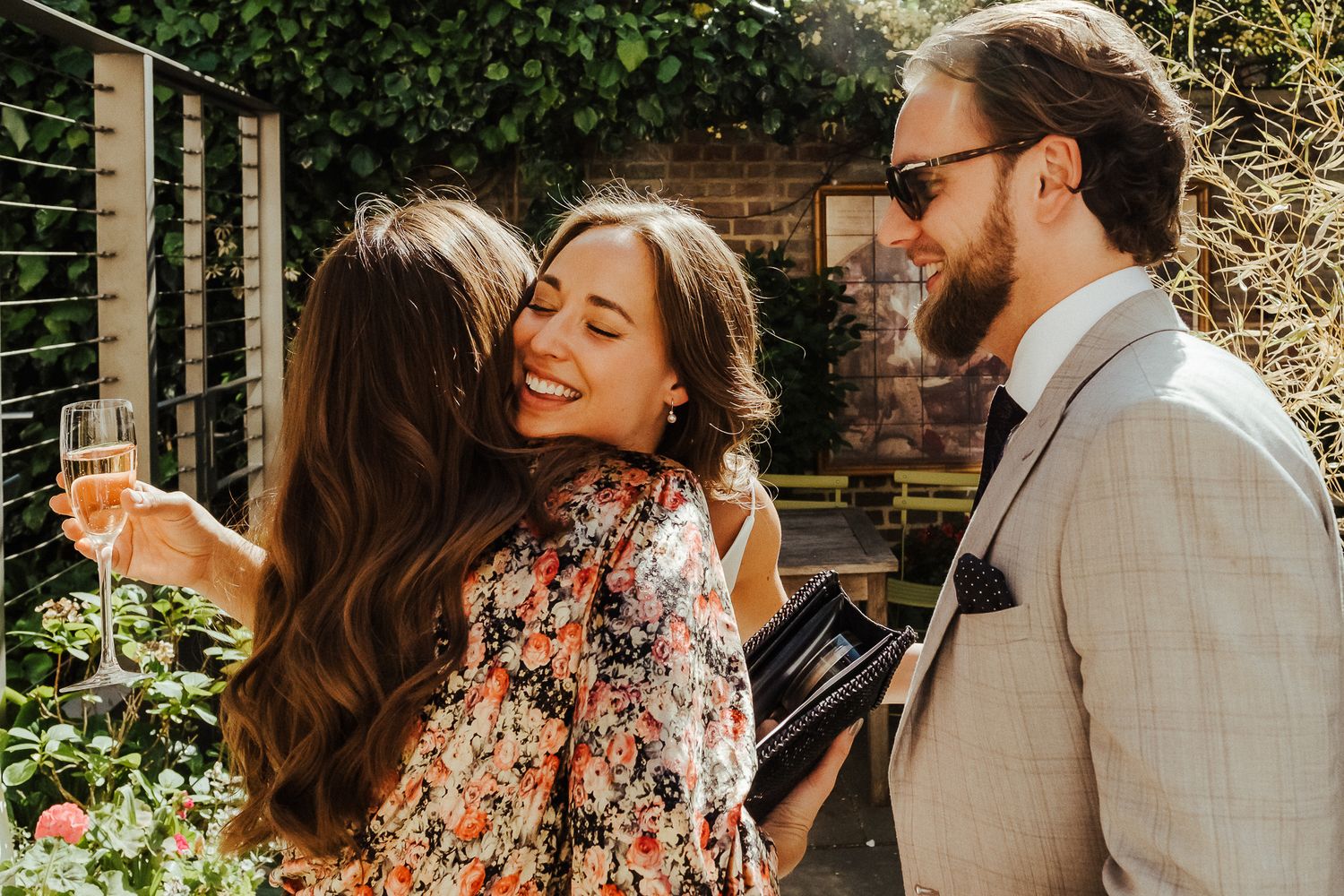 Friends share joyful moments and champagne in a sunny garden setting.
