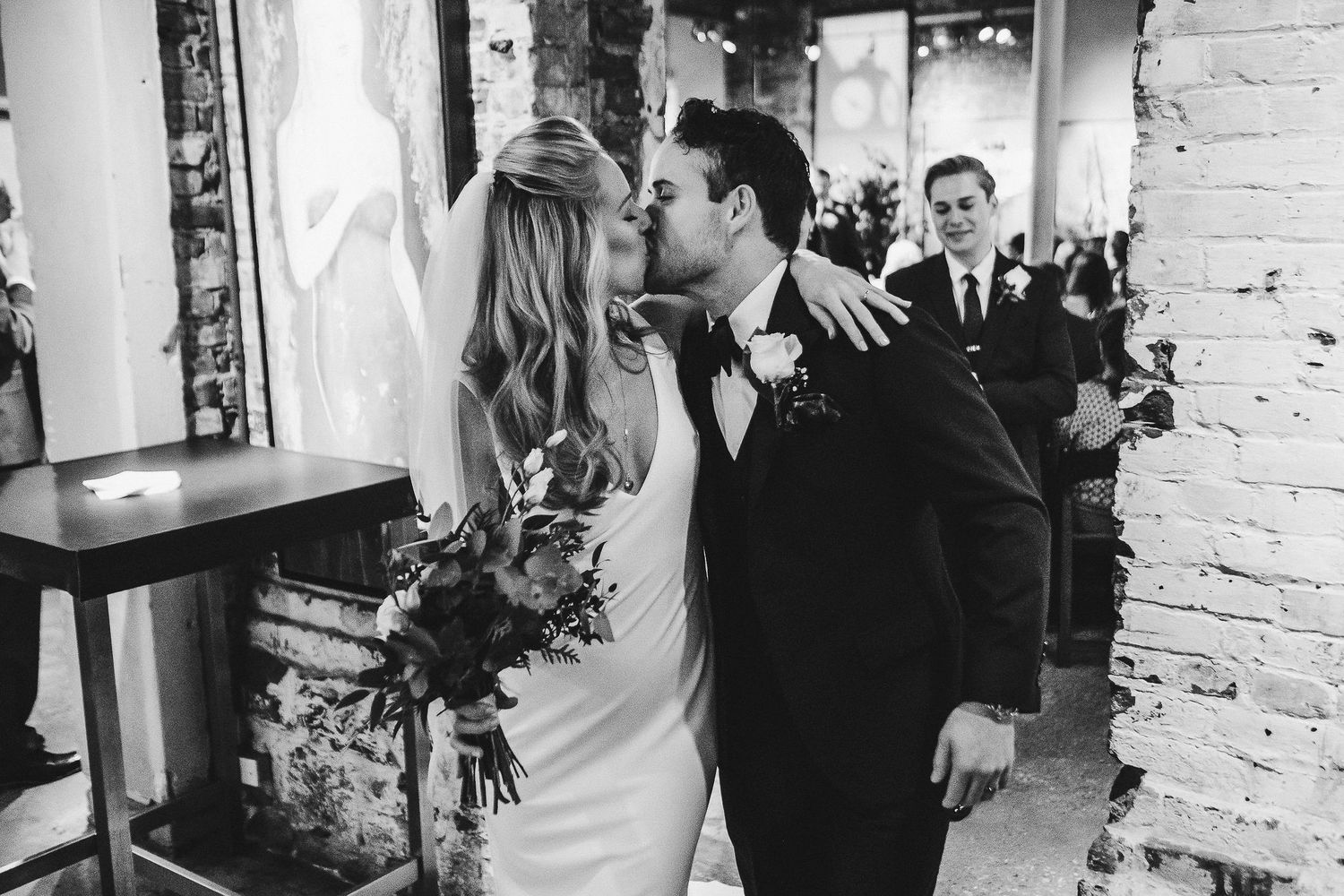 A romantic black and white wedding moment captured against a white brick wall background.