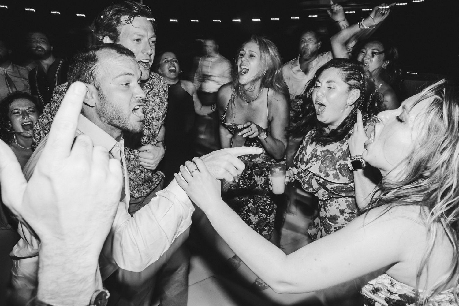 Black and white photo captures energetic dancing and celebration at a lively party.