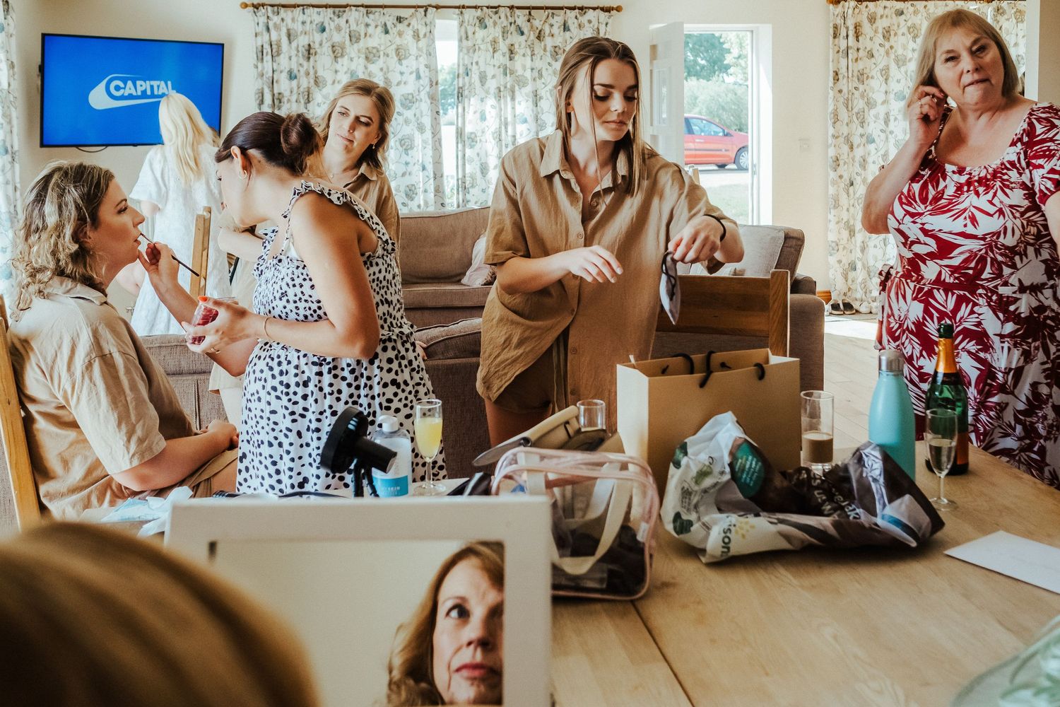 Group of friends laughing together while getting ready in a sunlit room with floral curtains.