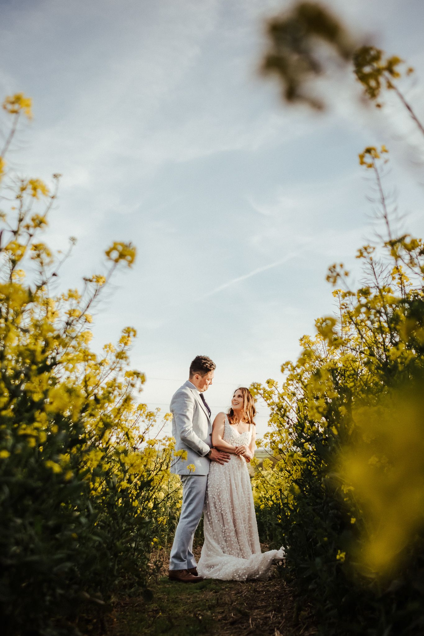 A romantic couple embraces in a field of yellow wildflowers during golden hour.