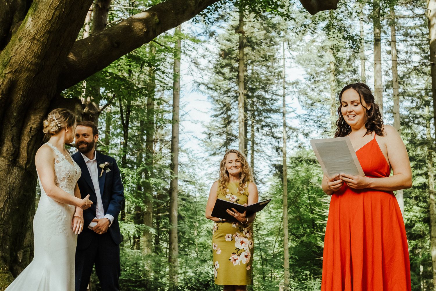 An outdoor forest wedding ceremony with attendants in formal attire under tall trees.