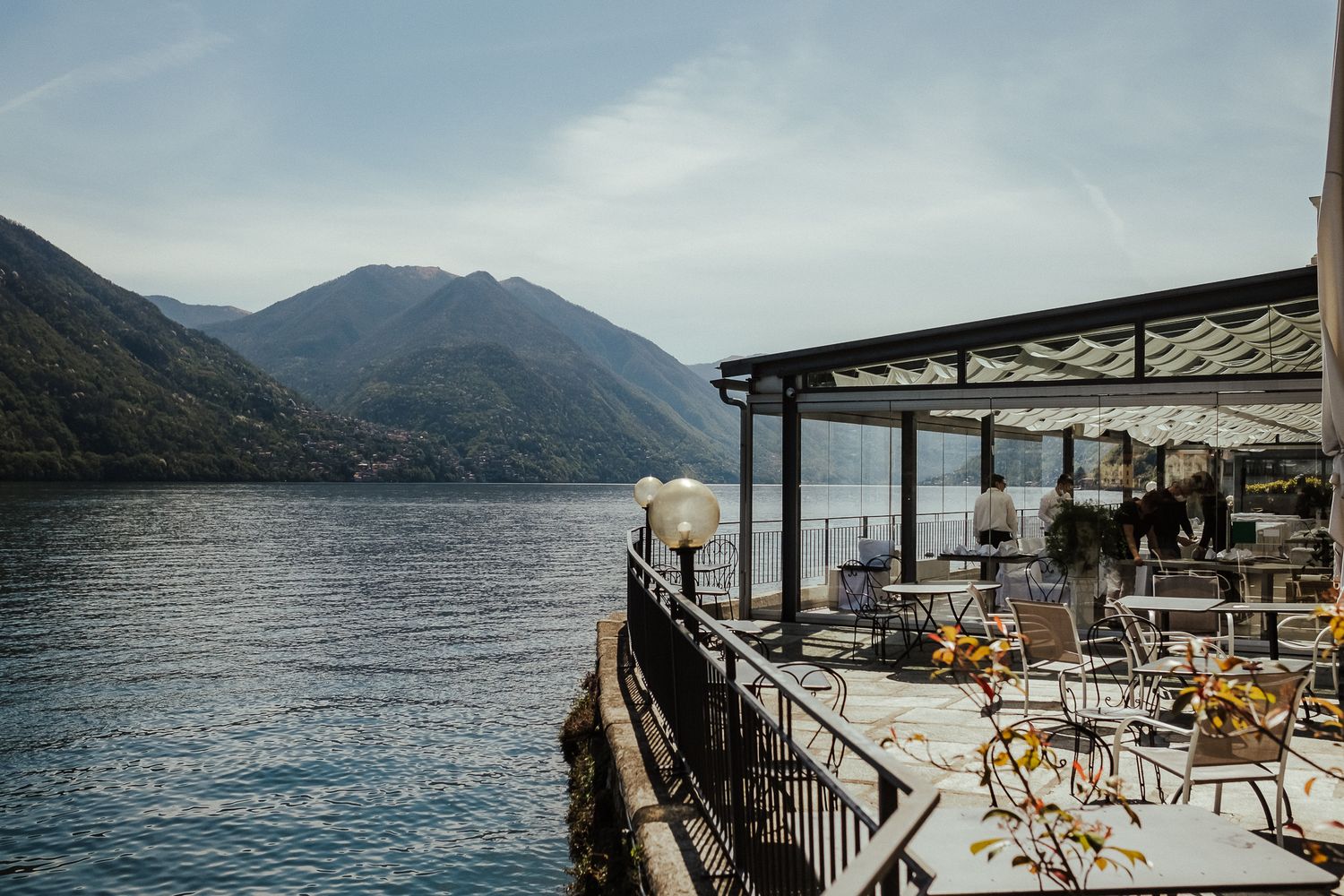Lakeside restaurant terrace with mountain views and empty tables and chairs.