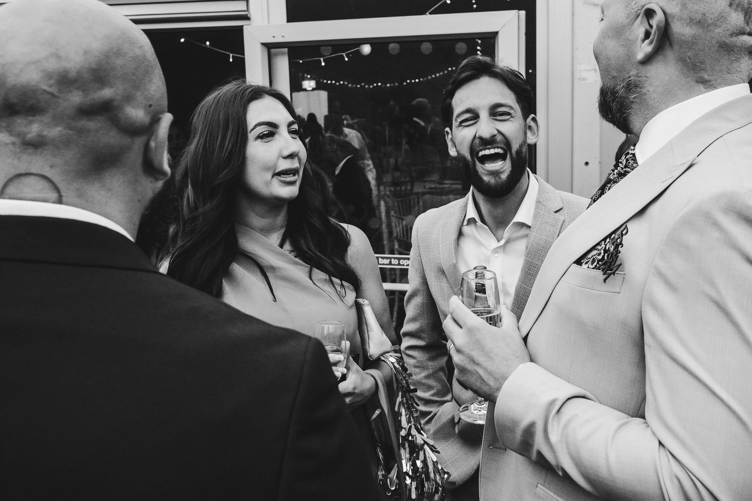 A group of guests enjoy a lively moment at a wedding reception, with laughter and smiles filling the frame.