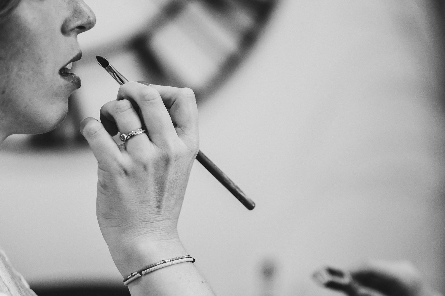 Black and white detail shots of hands during wedding preparation and makeup application.