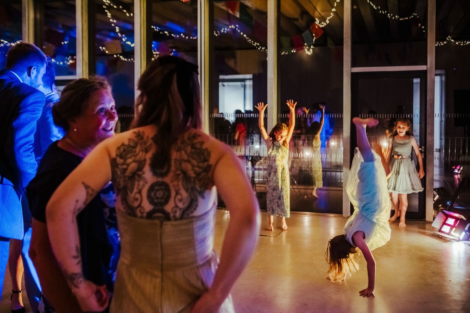 Wedding reception dance floor with guests dancing under blue lighting and string lights.