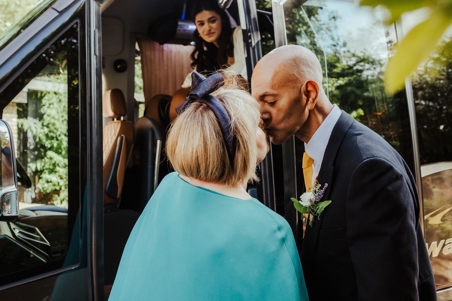 Wedding guests arriving at a vehicle with people greeting each other outside.