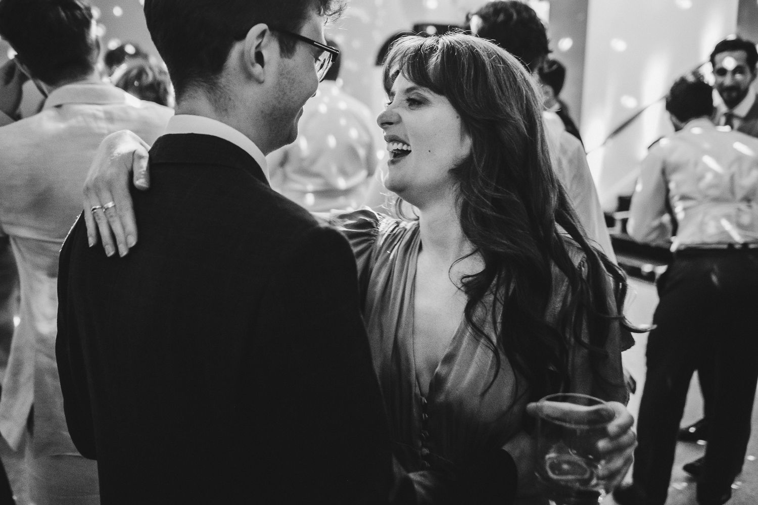 A candid black and white shot of two people dancing closely at an evening celebration.