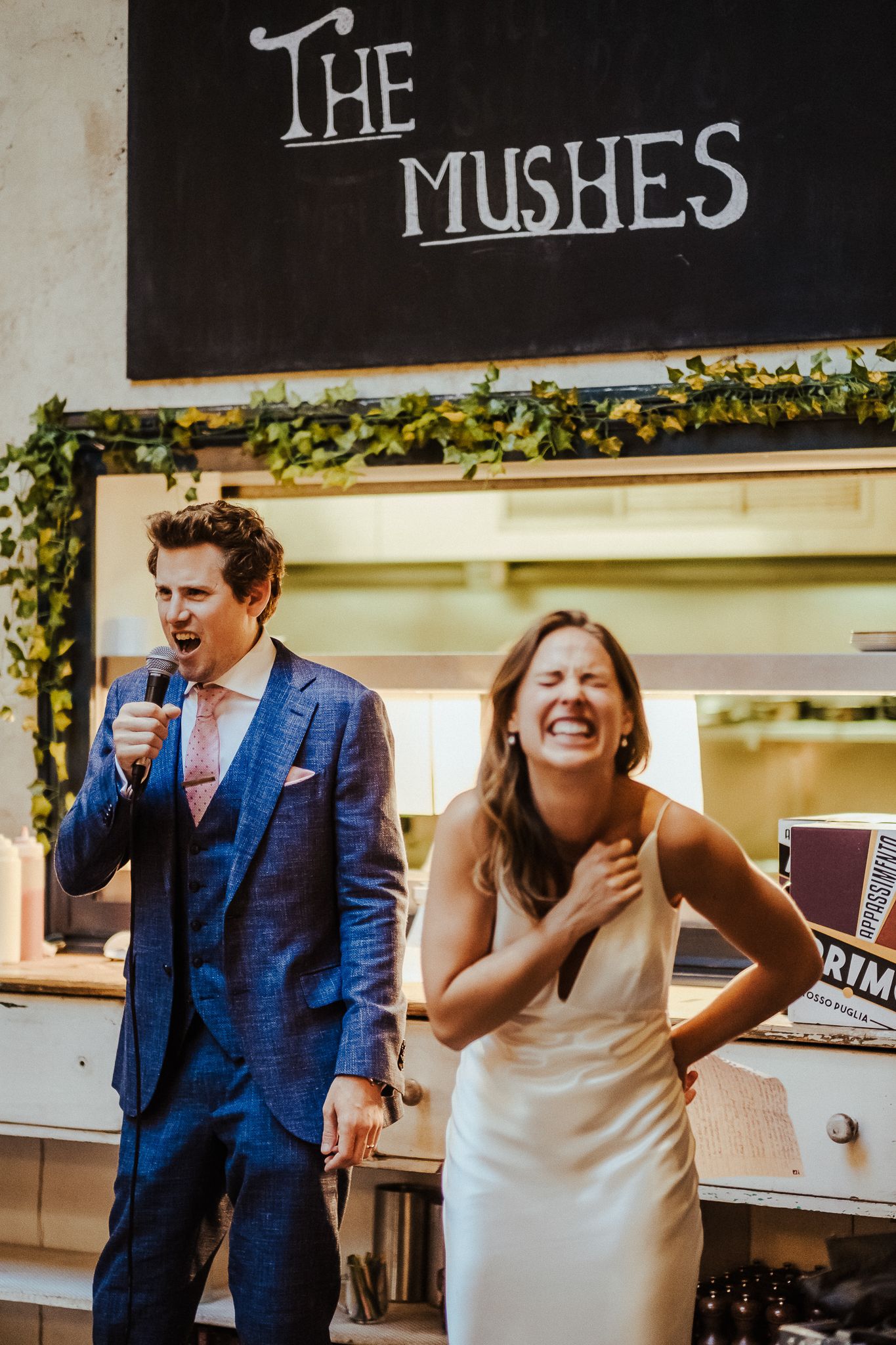 Joyful moment captured under 'The Mushes' sign at a wedding reception venue.