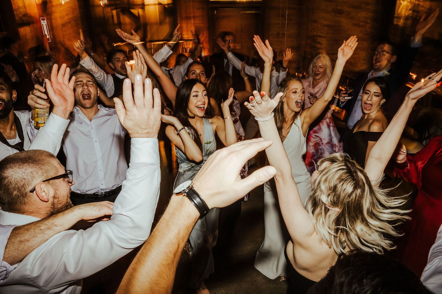 Dancing crowd with raised hands celebrating at a lively indoor party with rustic wood decor.