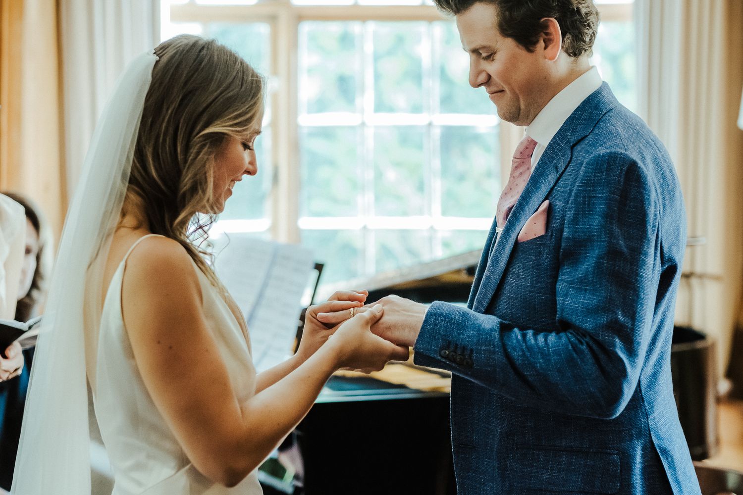 A couple exchanges rings by a window during their wedding ceremony.