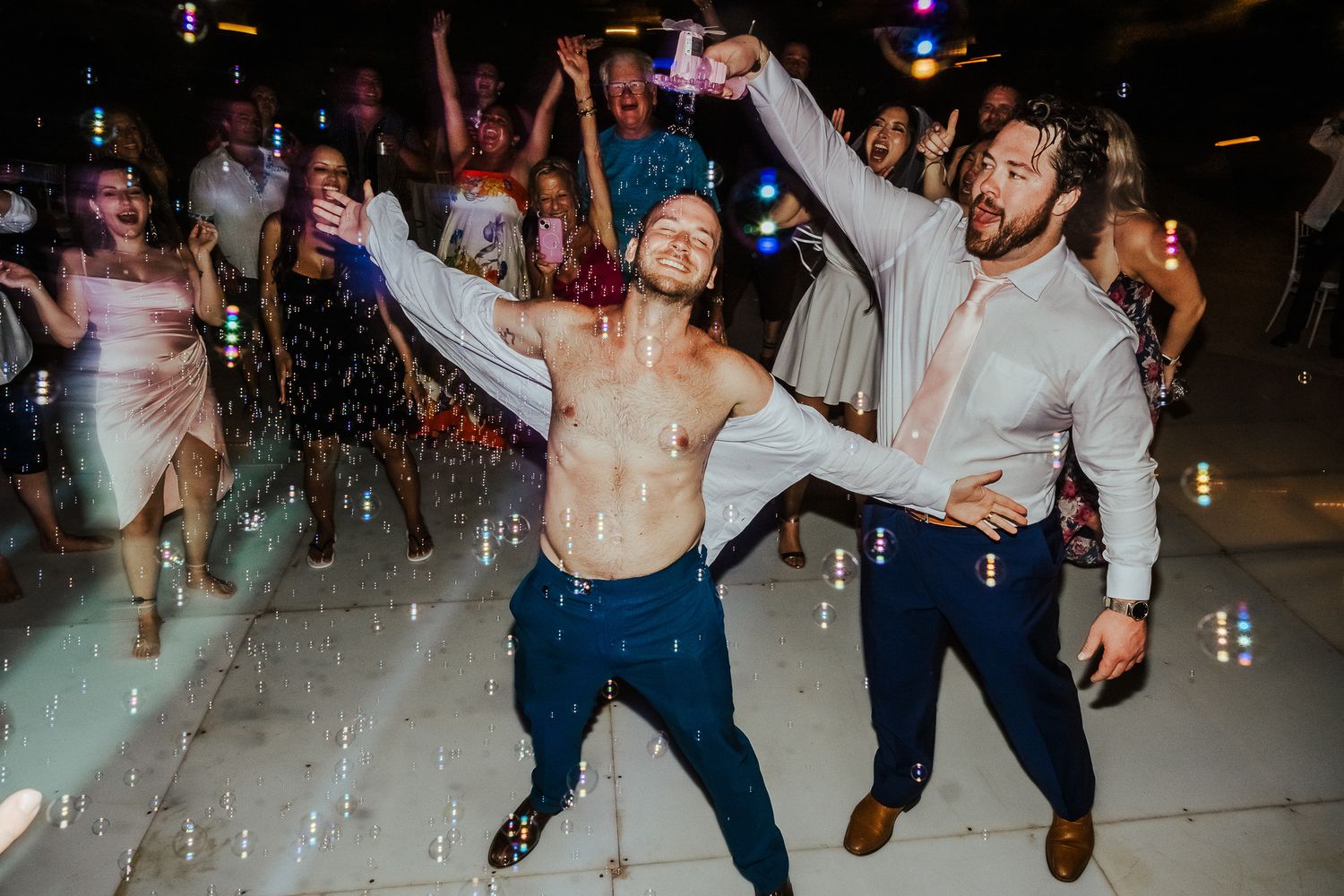Enthusiastic dancers celebrating on a reflective dance floor under party lights.