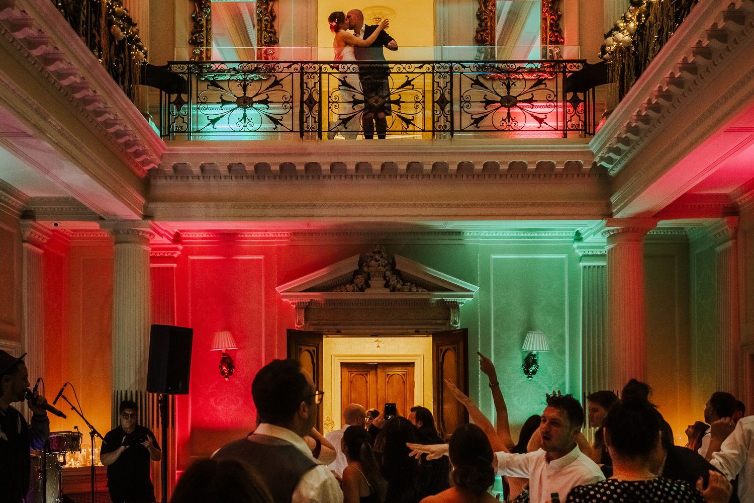 Ornate reception venue with dramatic colored uplighting and architectural details on ceiling.