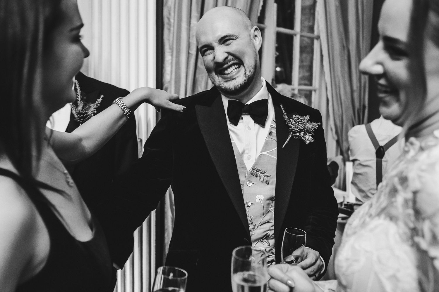 Black and white candid photo of guests enjoying conversation during a formal wedding reception.