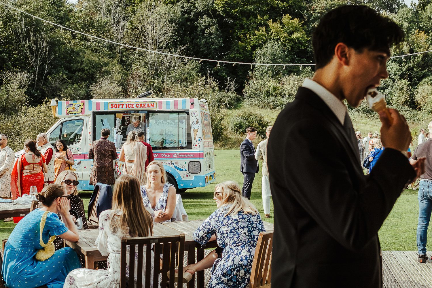 Outdoor wedding reception with guests gathered around tables and an ice cream truck in the background.